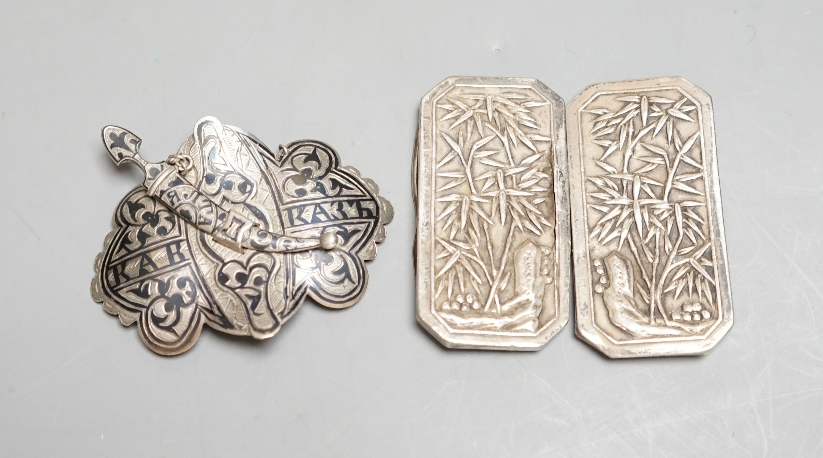 A Chinese white metal belt buckle by Wang Hing(a.f.)68mm and a Russian silver and niello work belt buckle.